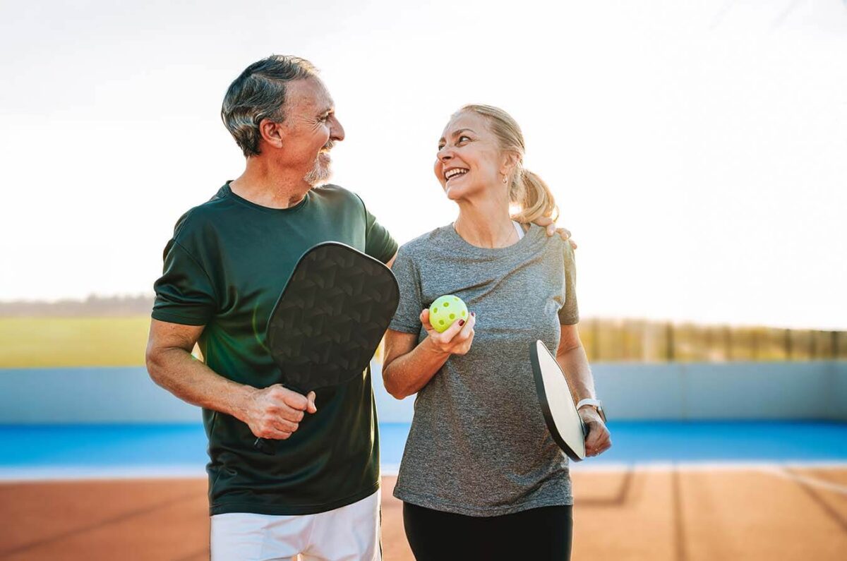 Older couple smiling as they play pickle ball together.